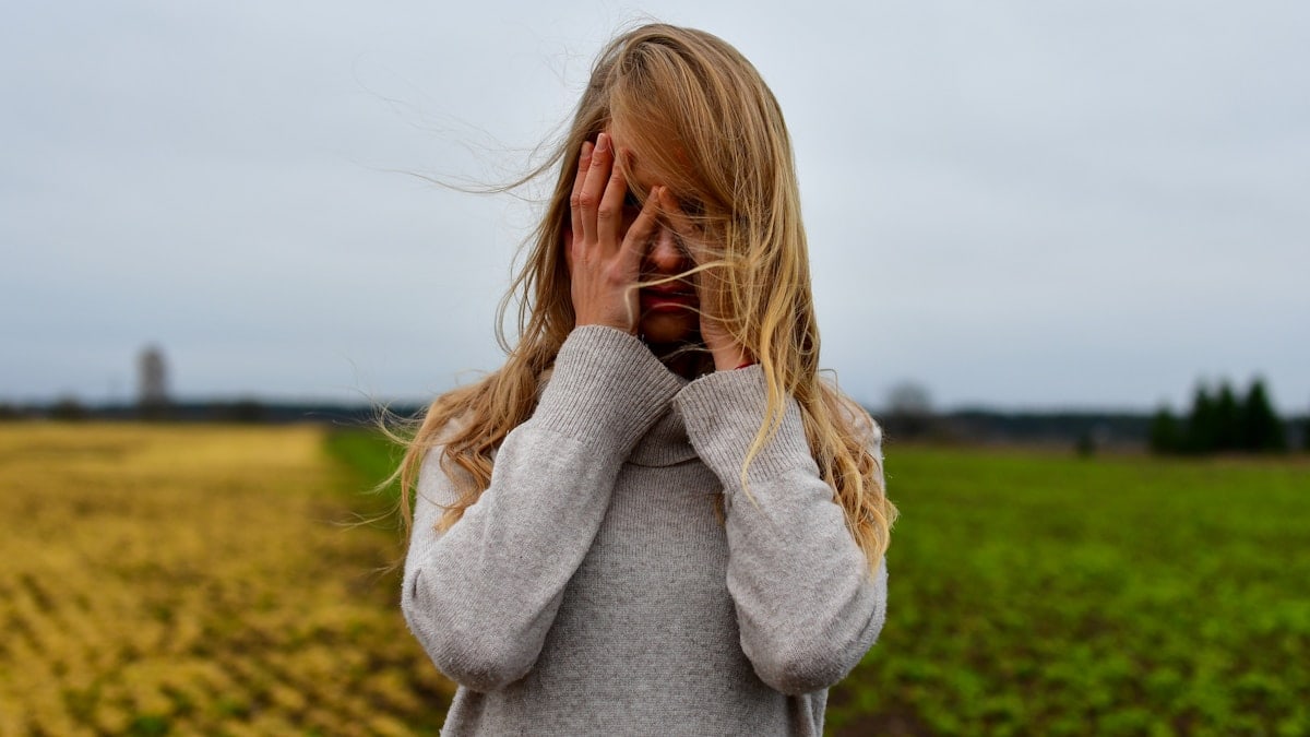 Young woman in a cozy knit sweater standing in a windy autumn field with hair blowing across her face.